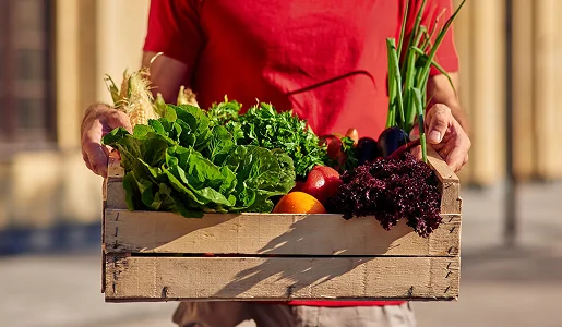 homme avec t-shirt rouge qui tient une cagette de légumes frais